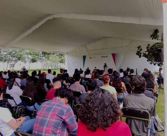 Estudiantes de nuevo ingreso sentadxs, mirando hacia el podio.