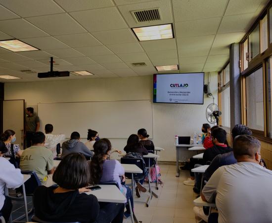 estudiantes en butacas con una televisión al fondo en la que se lee el texto CUTLAJO